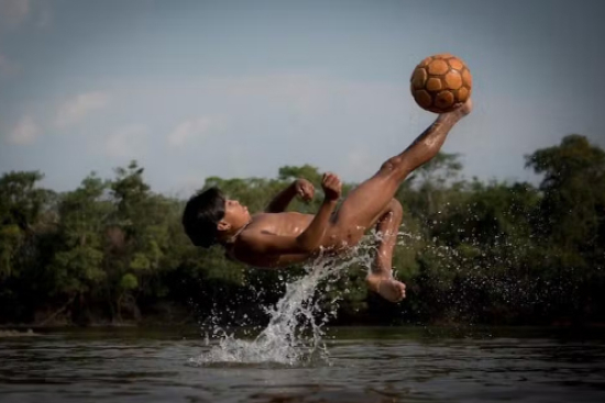 Imagem de criança indígena fazendo bicicleta em rio de MT vence concurso nacional de fotografia